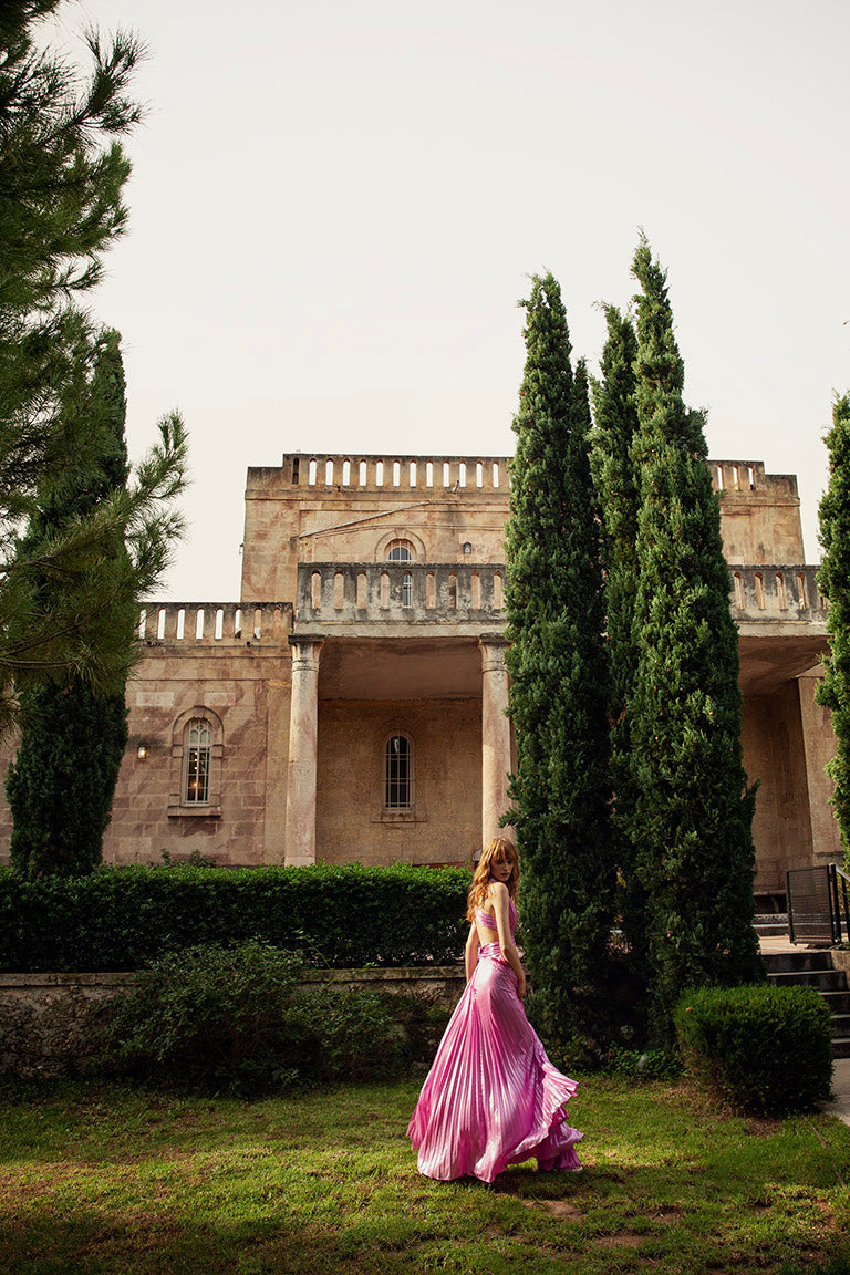 Femme en robe rose marchant devant un château, vêtue d’une robe de bal rose, danseuse étoile dans la roseraie, longue robe fluide luxueuse