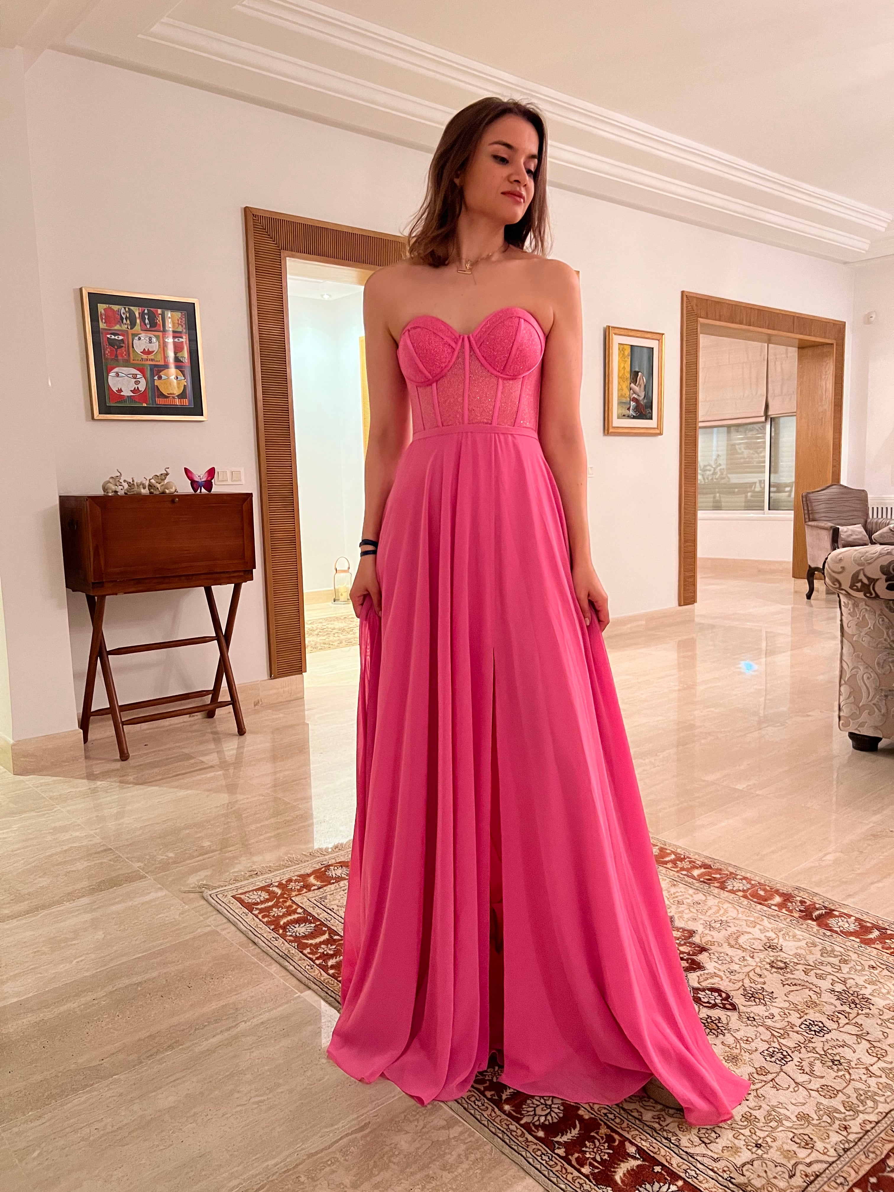 femme dans une robe rose debout dans un salon, robe bustier, robe rose, robe ouverte, robe de bal rose brillant, robe extravagante, robe fluide, robe légère à moitié ouverte